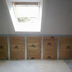 Unfinished attic with insulation panels along a wall and a skylight overhead letting in natural light.