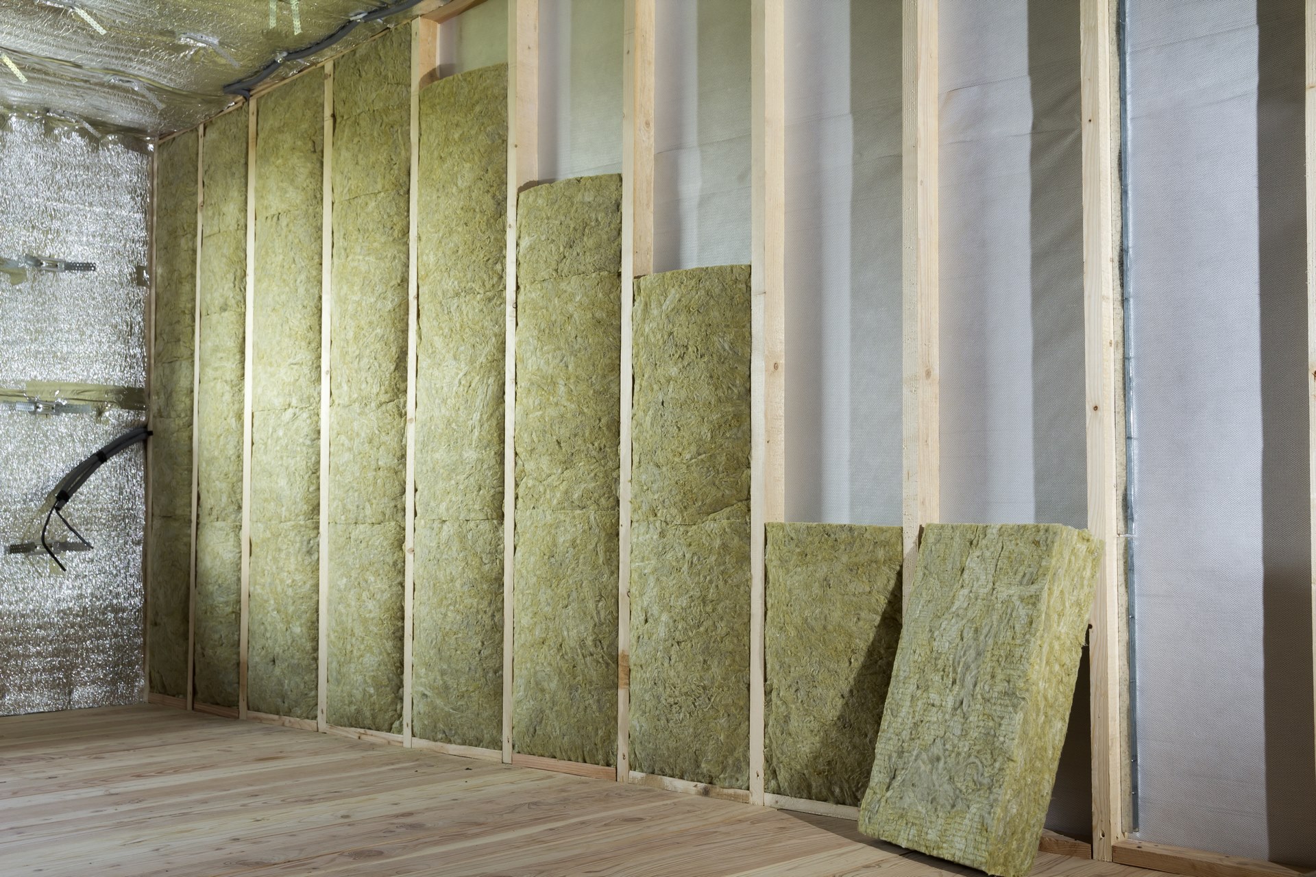 Unfinished wall framing with vertical studs and mineral wool insulation between them; foil-covered ductwork visible on the left side.