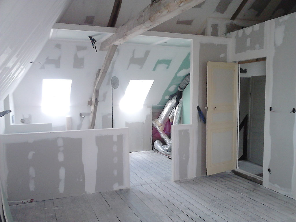 Unfinished attic renovation with taped drywall seams, slanted ceiling and exposed wooden beam