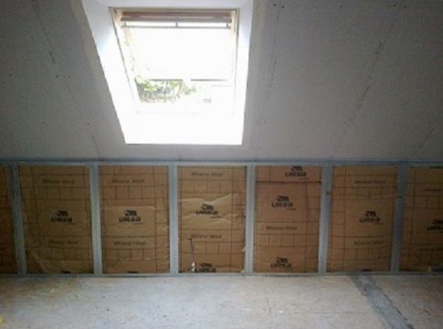 Unfinished attic with insulation panels along a wall and a skylight overhead letting in natural light.