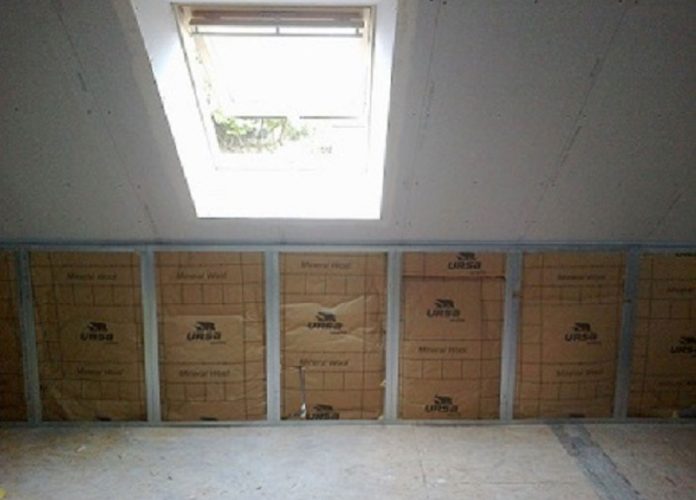 Unfinished attic with insulation panels along a wall and a skylight overhead letting in natural light.