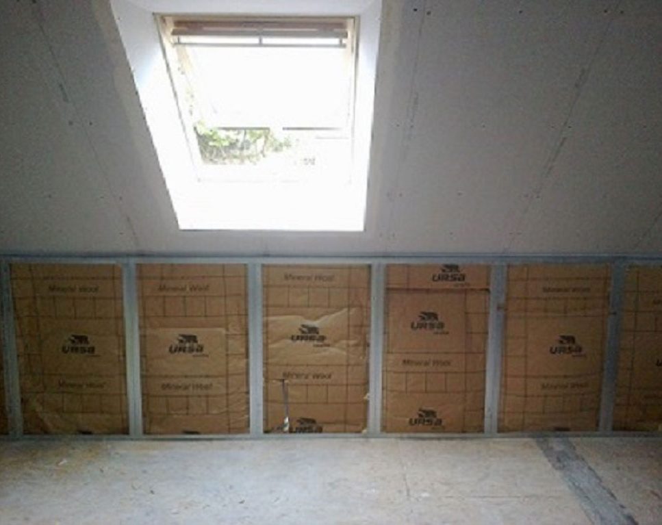 Unfinished attic with insulation panels along a wall and a skylight overhead letting in natural light.