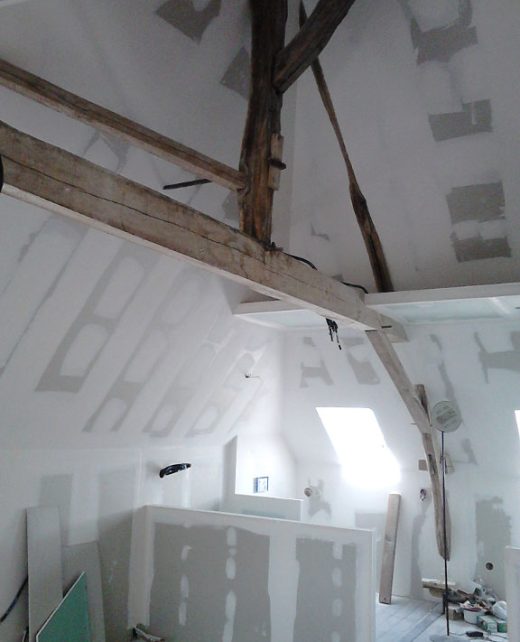 Attic renovation in progress with white drywall panels, exposed wooden rafters, and a skylight letting in daylight.