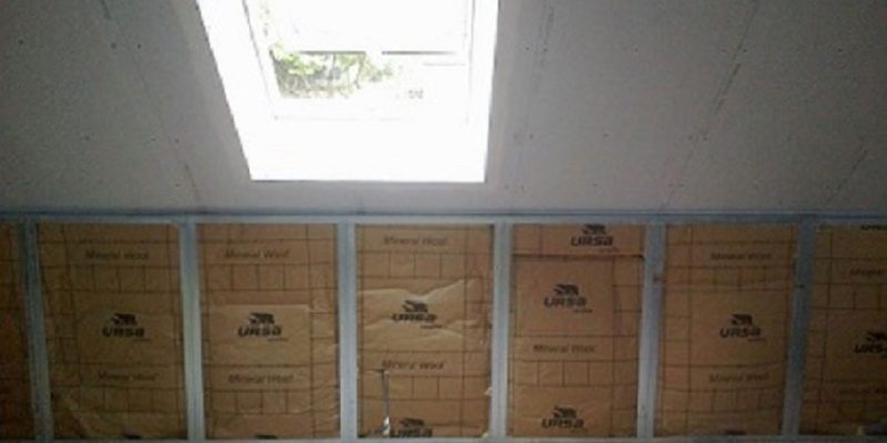 Unfinished attic with insulation panels along a wall and a skylight overhead letting in natural light.